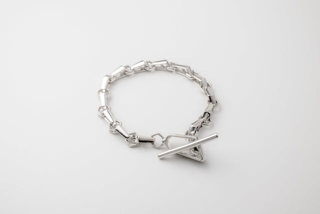 Polished 925 silver bracelet of faceted hexagonal links with a T-bar clasp, laid in a circle on light grey, seen from above.