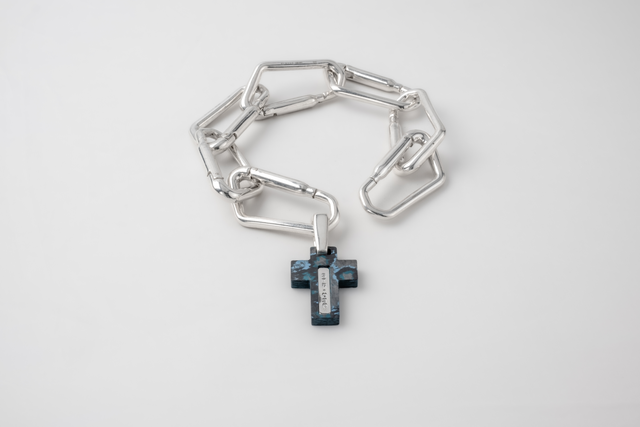 Silver carabiner-link bracelet with a dark stone cross hanging from the clasp.