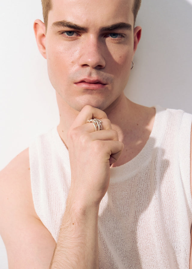 Silver chain-link ring on a man's fist raised to his chin, white knit tank, pale studio wall in daylight — STRUGA