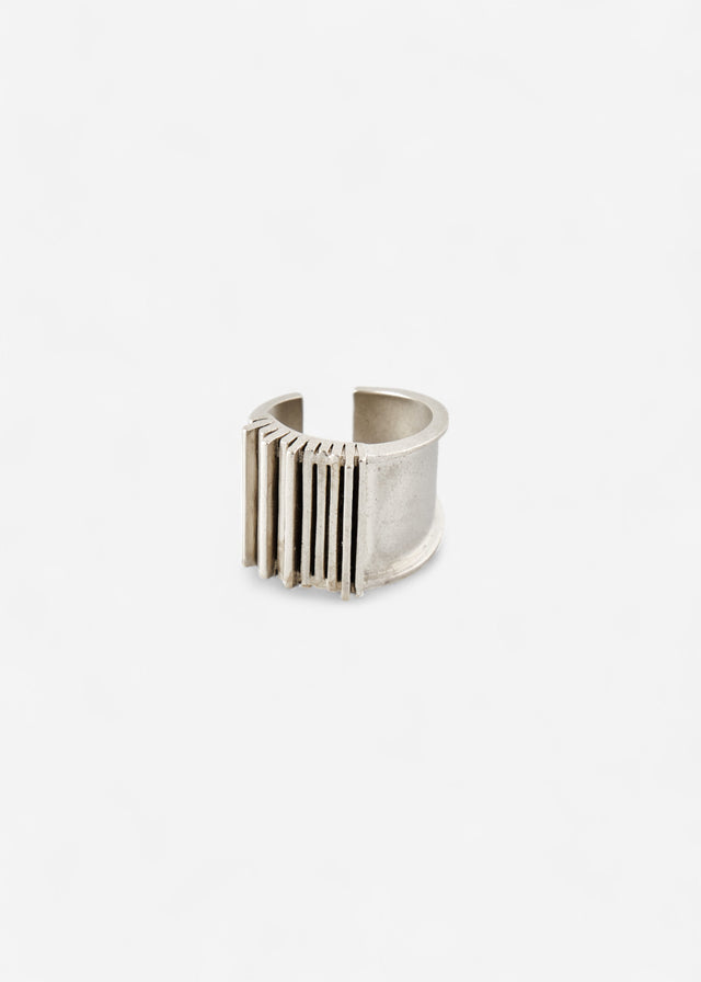 Wide silver Brutalism cuff head-on, its ribbed bars standing off the band, pale ground — STRUGA