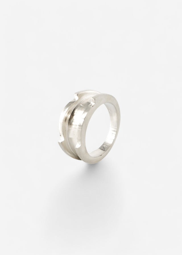 Wide cool white metal ring, ridged crest and notched points on the edges, mirror highlights, plain white backdrop — STRUGA