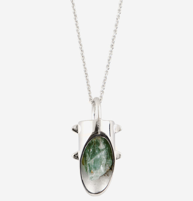 Silver amulet pendant on a fine chain: spiked capsule holding an uncut green crystal behind a window.