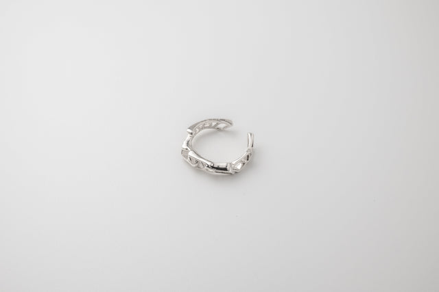 Open-ended silver ring of sculpted links, polished white metal, angled on a pale grey studio backdrop — STRUGA