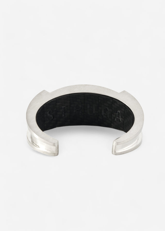 Open silver cuff shot head-on, flared polished ends, black carbon-weave panel with raised STRUGA letters, on white — STRUGA